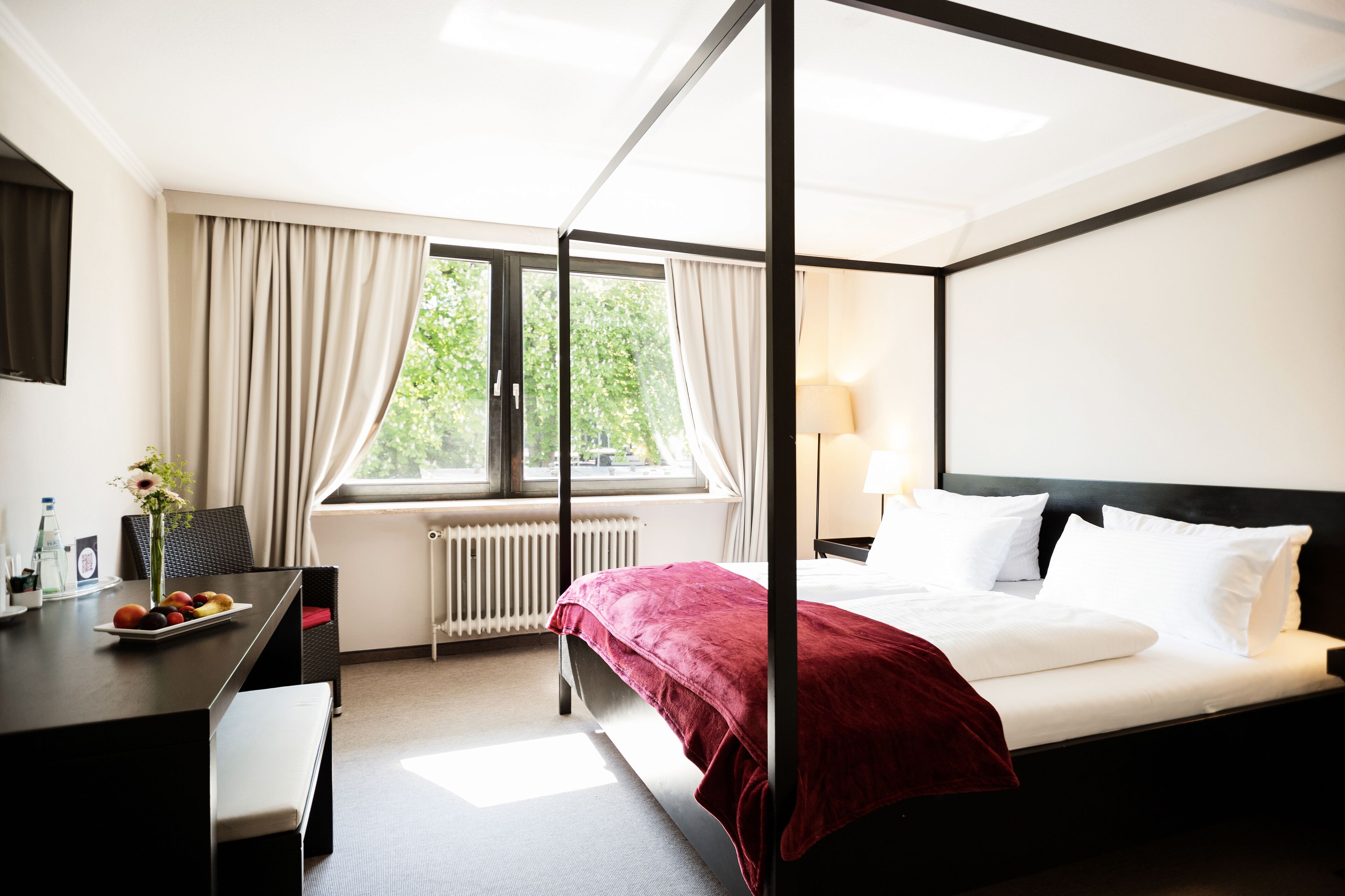 Un lit à baldaquin avec du linge de lit blanc, un plaid rouge et une table de chevet avec une lampe.