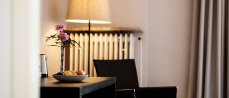 A hotel room with a table, a lamp, a chair, and a radiator.