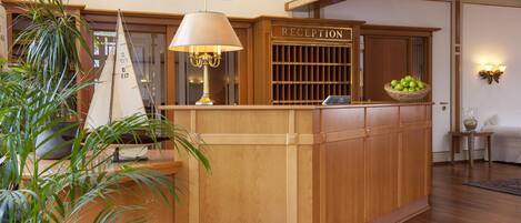 A reception desk with a wooden finish, a lamp, a sign reading "RECEPTION", and a basket of apples.