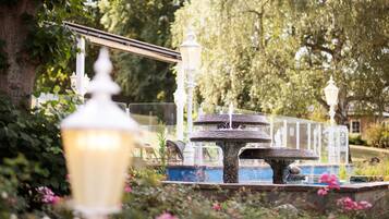 A fountain with multiple tiers and a lamp post in a garden setting.