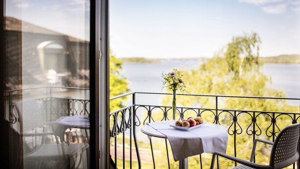 Un balcon avec une table dressée pour deux personnes, donnant sur un lac et des arbres.