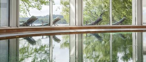 A pool with lounge chairs and a view of trees and a lake.
