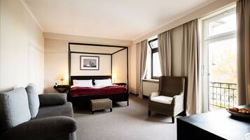 A hotel room with a four-poster bed, a sofa, a chair, and a view of the outdoors through a window.
