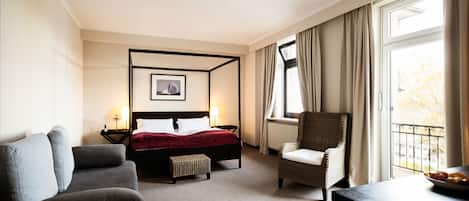 A hotel room with a four-poster bed, a sofa, a chair, and a view of the outdoors through a window.