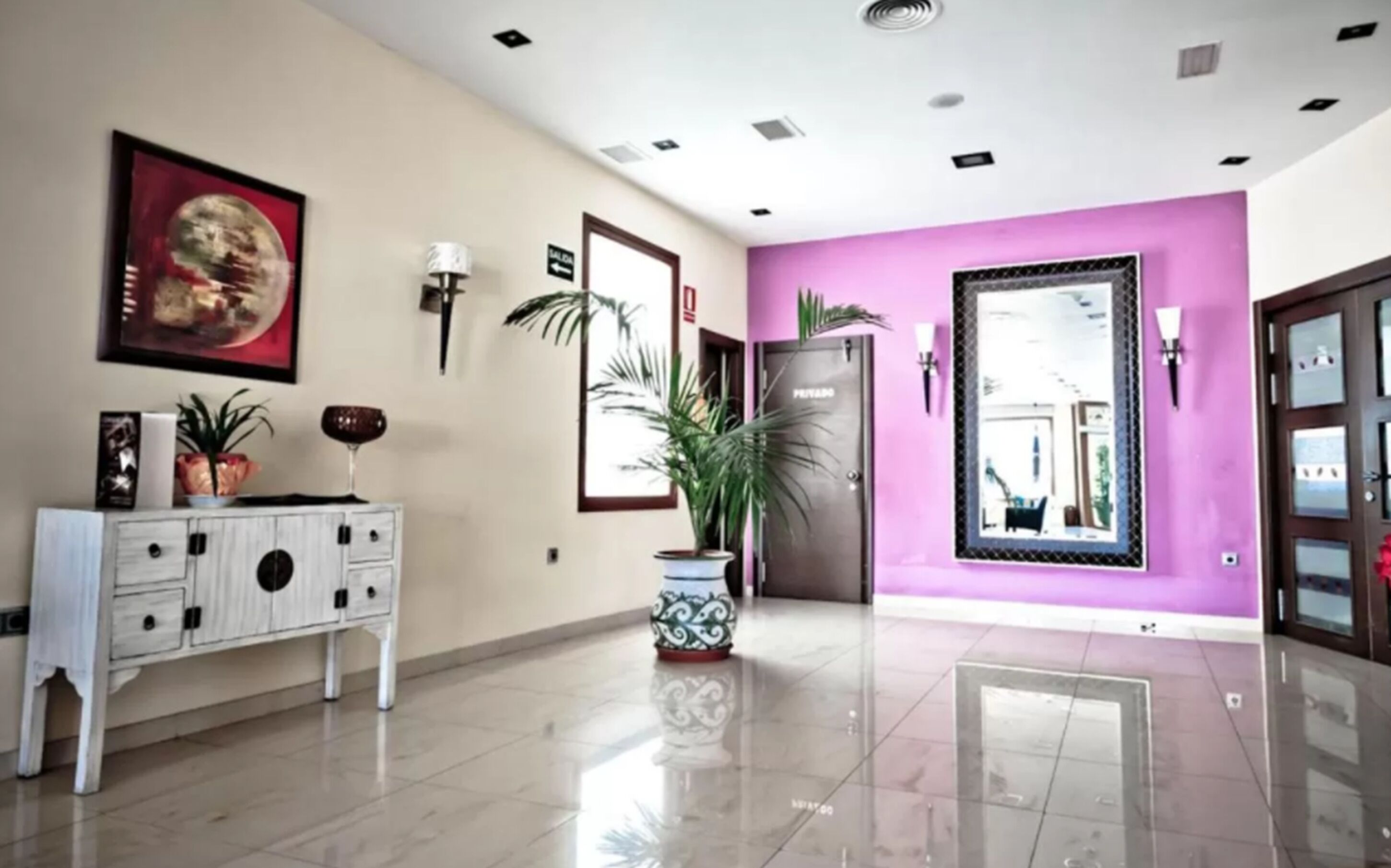 Un moderno vestíbulo de hotel con una consola blanca, una planta grande en maceta, una obra de arte enmarcada y una pared de acento morada.
