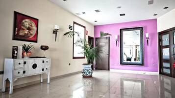 Un moderno vestíbulo de hotel con una consola blanca, una planta grande en maceta, una obra de arte enmarcada y una pared de acento morada.