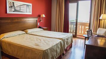 A hotel room with two beds, a desk, a chair, a lamp, a phone, and a window with curtains.