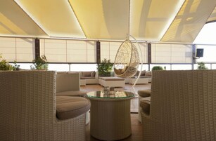Un área de estar moderna con muebles de mimbre, una silla colgante y una mesa de centro de vidrio.
