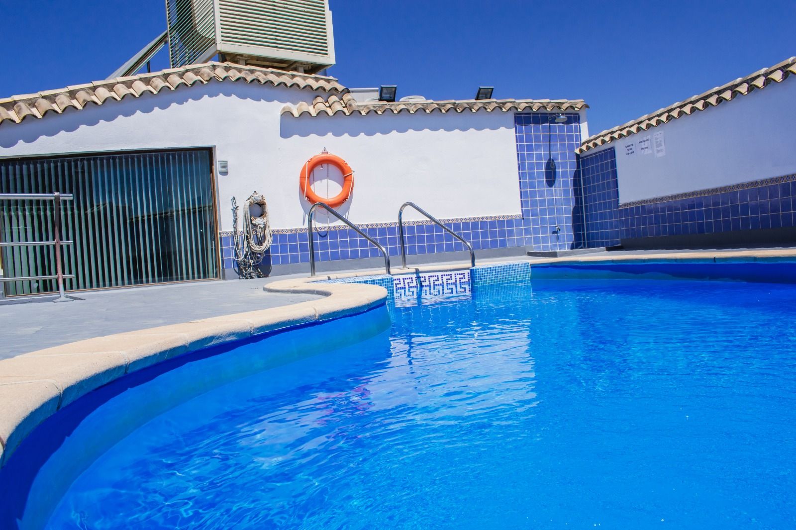 Una piscina con un flotador salvavidas, una escalera metálica y un muro de azulejos.