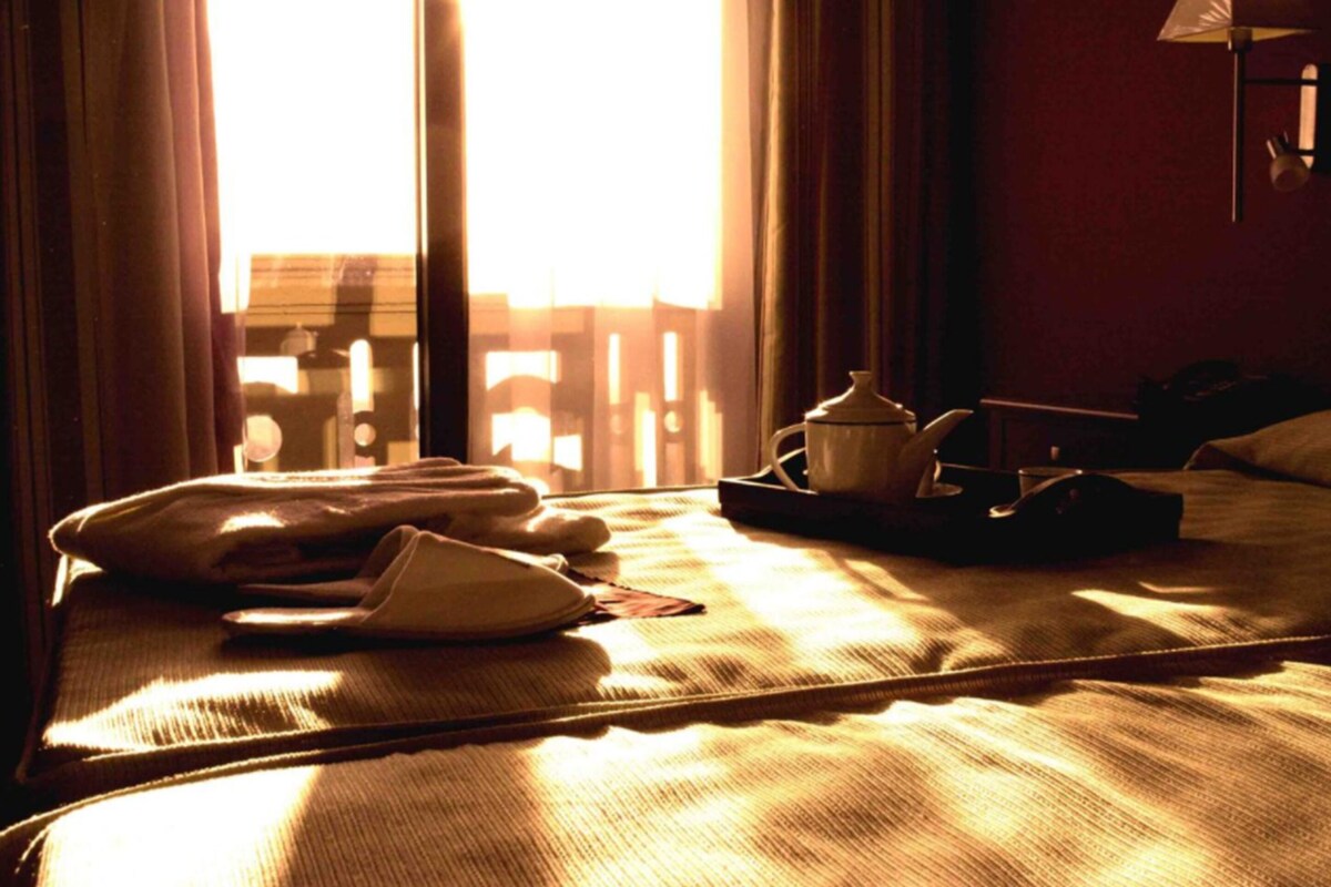 A hotel room with a bed, a nightstand, a lamp, and a window with curtains.