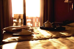 Habitación de hotel con una cama, una mesita de noche, una lámpara y un ventanal con cortinas.