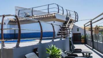 Una terraza en la azotea con piscina, sillas de descanso y un espacio de estar techado.