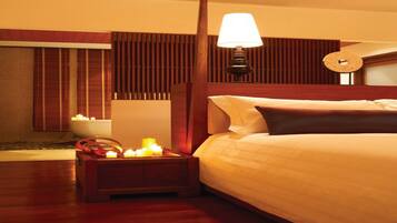 A hotel room with a wooden bed, a nightstand with candles, a wall clock, and a window with blinds.