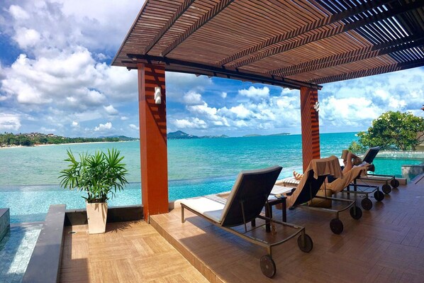 A covered outdoor area with lounge chairs and a potted plant, overlooking a clear blue sea and distant land. - The Sarann Koh Samui, Suites & Villas (Koh Samui)