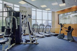 Uma academia com máquinas de cardio, equipamentos de musculação e amplas janelas com vista para a cidade.