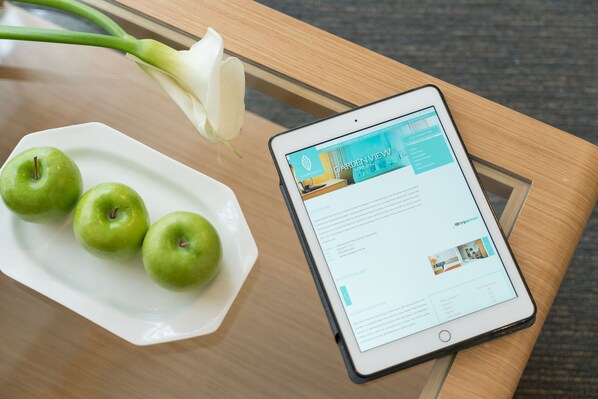 A tablet displaying a website on a wooden table with a white plate of green apples and a white flower. - Garden View Hong Kong (Hong Kong)