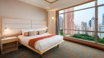 A hotel room with a large bed, a nightstand, a desk, and a view of the cityscape.