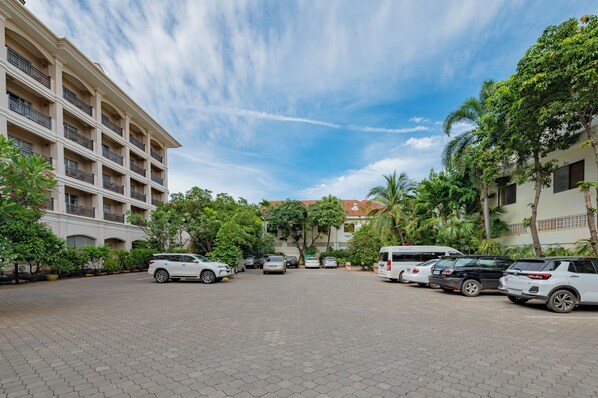 A parking area with multiple cars and a bus, surrounded by buildings and greenery. - Hotel Somadevi Angkor Resort & Spa (Siem Reap)
