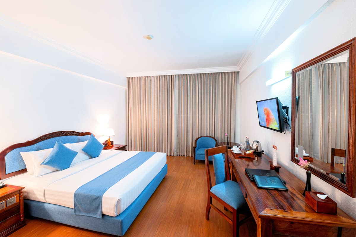 A hotel room with a large bed, a desk with a laptop, a chair, a mirror, and curtains.