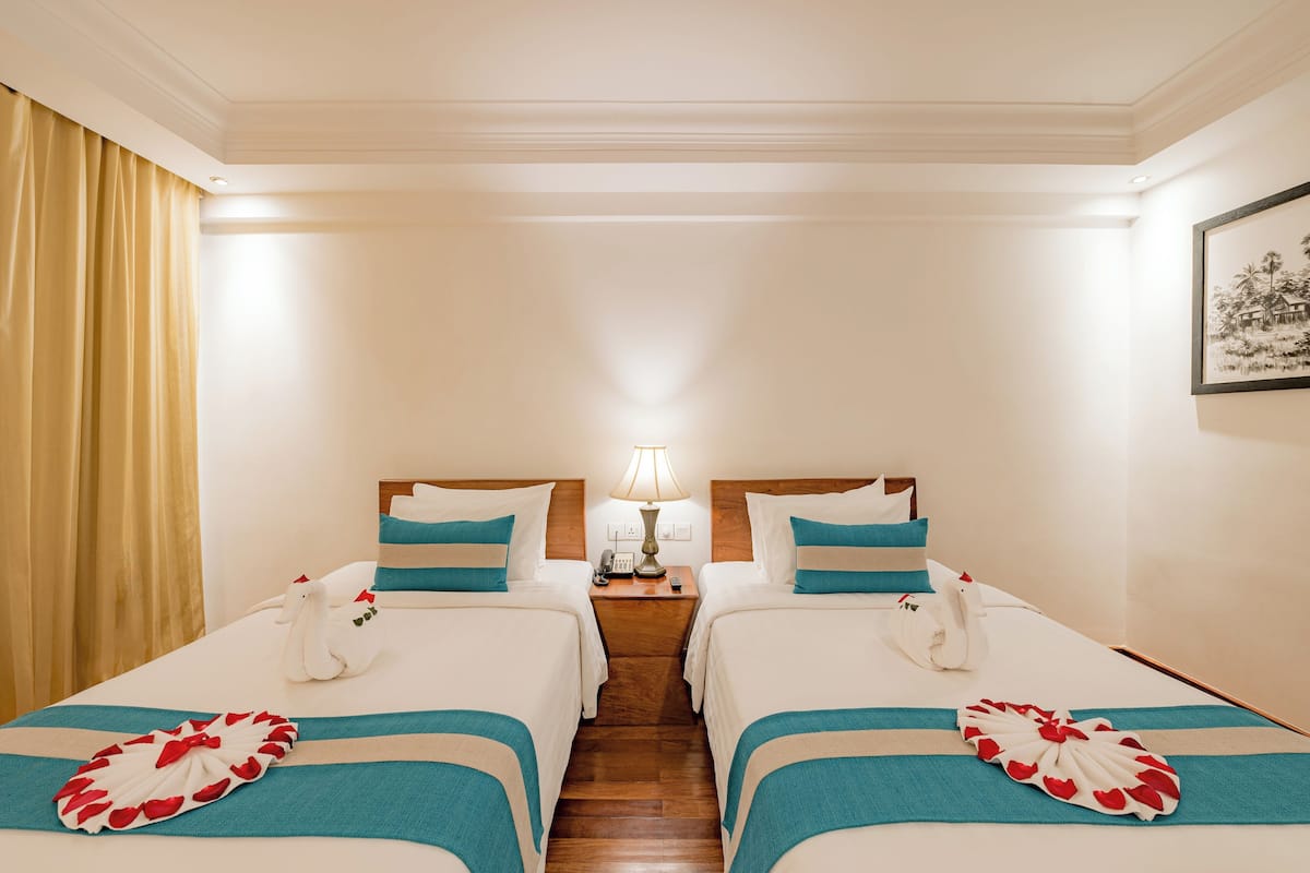 A hotel room with two beds, a nightstand with a lamp, and a framed picture on the wall.