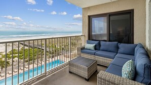A balcony with a view of the ocean, a pool, and a blue sofa.