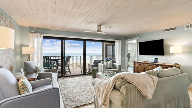A living room with a sofa, armchairs, a TV, and a view to the outside.