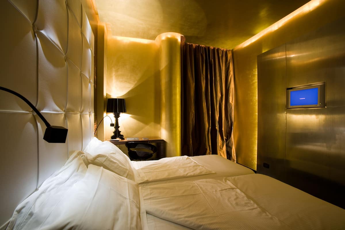 A hotel room with a bed, a bedside table, a lamp, a TV, and a curtain.