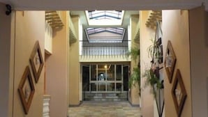 Un vestíbulo de hotel con una escalera central, tragaluces y cuadros en las paredes.