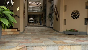 Pasillo con suelo de piedra que conduce a la entrada de un edificio, con balcón y detalles decorativos en la pared.