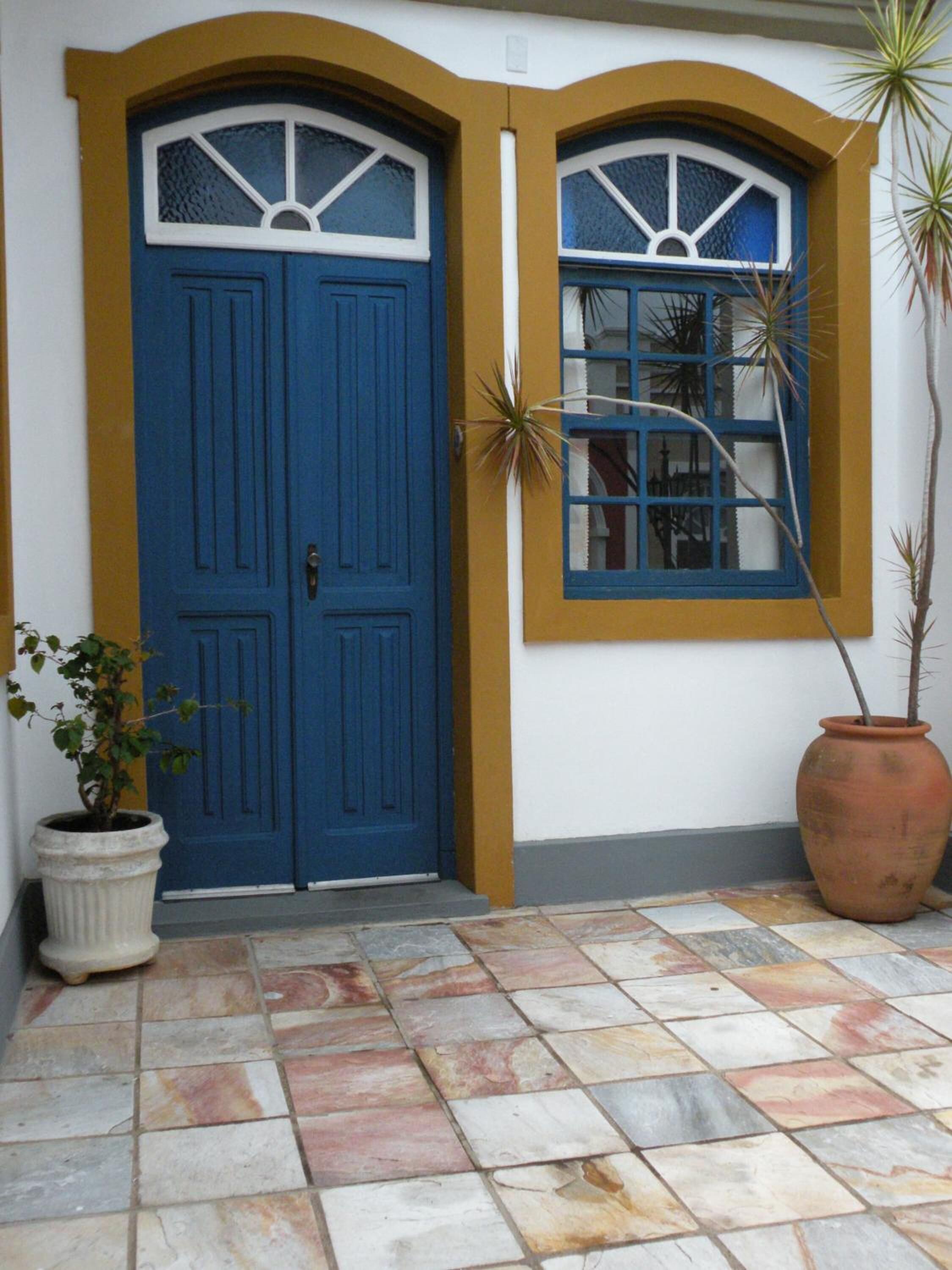 A blue door with a window, a potted plant, and a large terracotta pot.