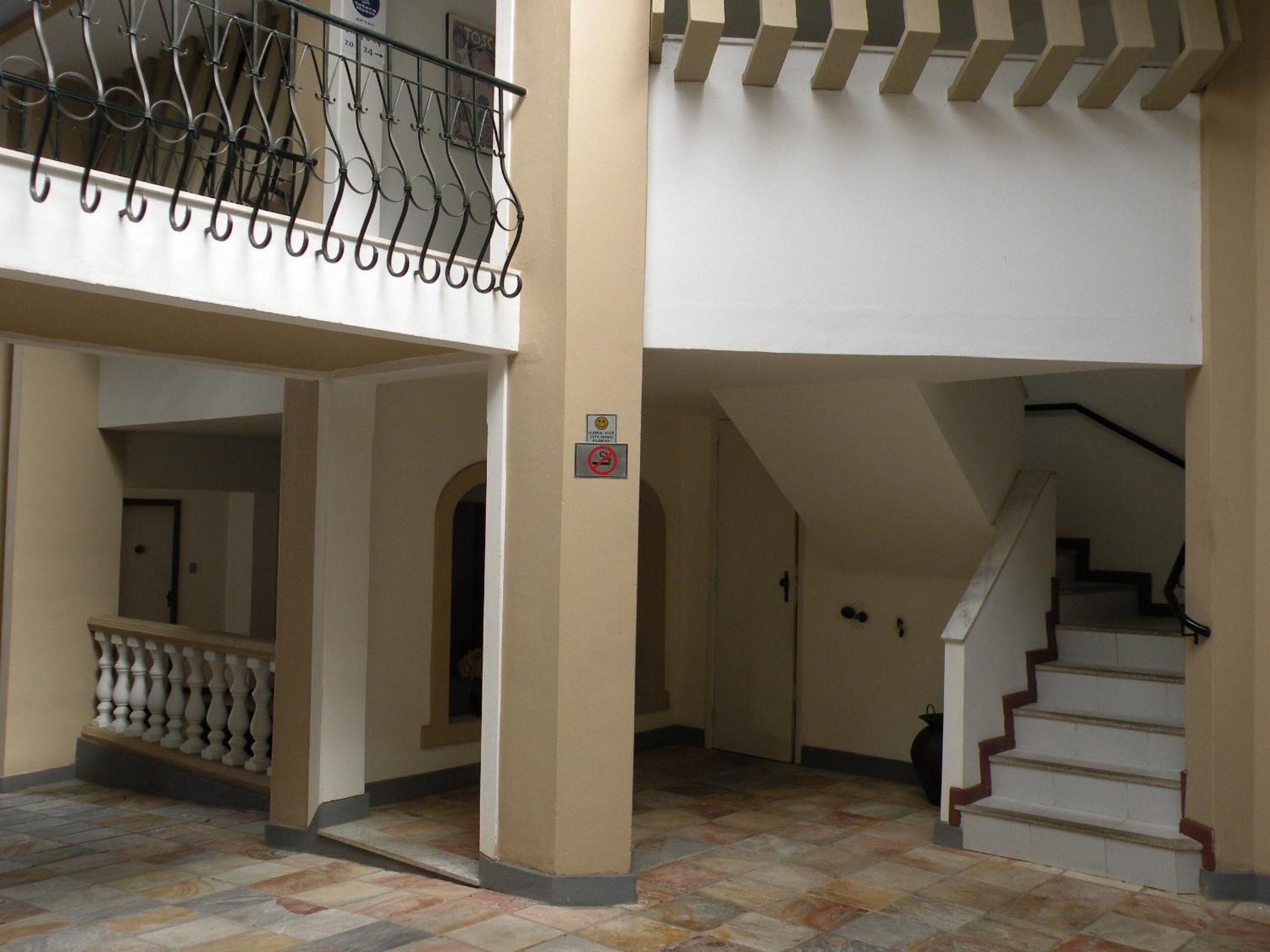 Un interior espacioso con una escalera, un balcón con barandillas metálicas y piso de baldosas.