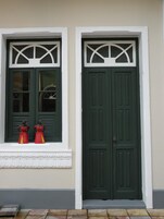 Un edificio con dos puertas verdes y ventanas con detalles blancos.