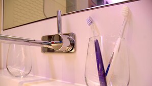 Ein Badezimmer mit einem Glas, das zwei Zahnbürsten hält, einem Chrom-Wasserhahn und einem Spiegel.
