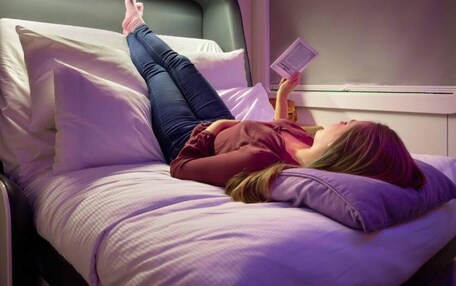 A person lying on a bed in a room with a window and a nightstand.