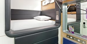Un lit compact avec un oreiller, un panneau de commande avec des boutons et un petit compartiment de rangement.