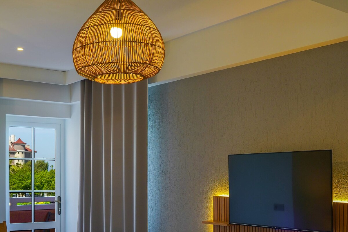 Habitación de hotel con una cama grande, un televisor montado en la pared, una lámpara de techo y vistas al exterior a través de una puerta.