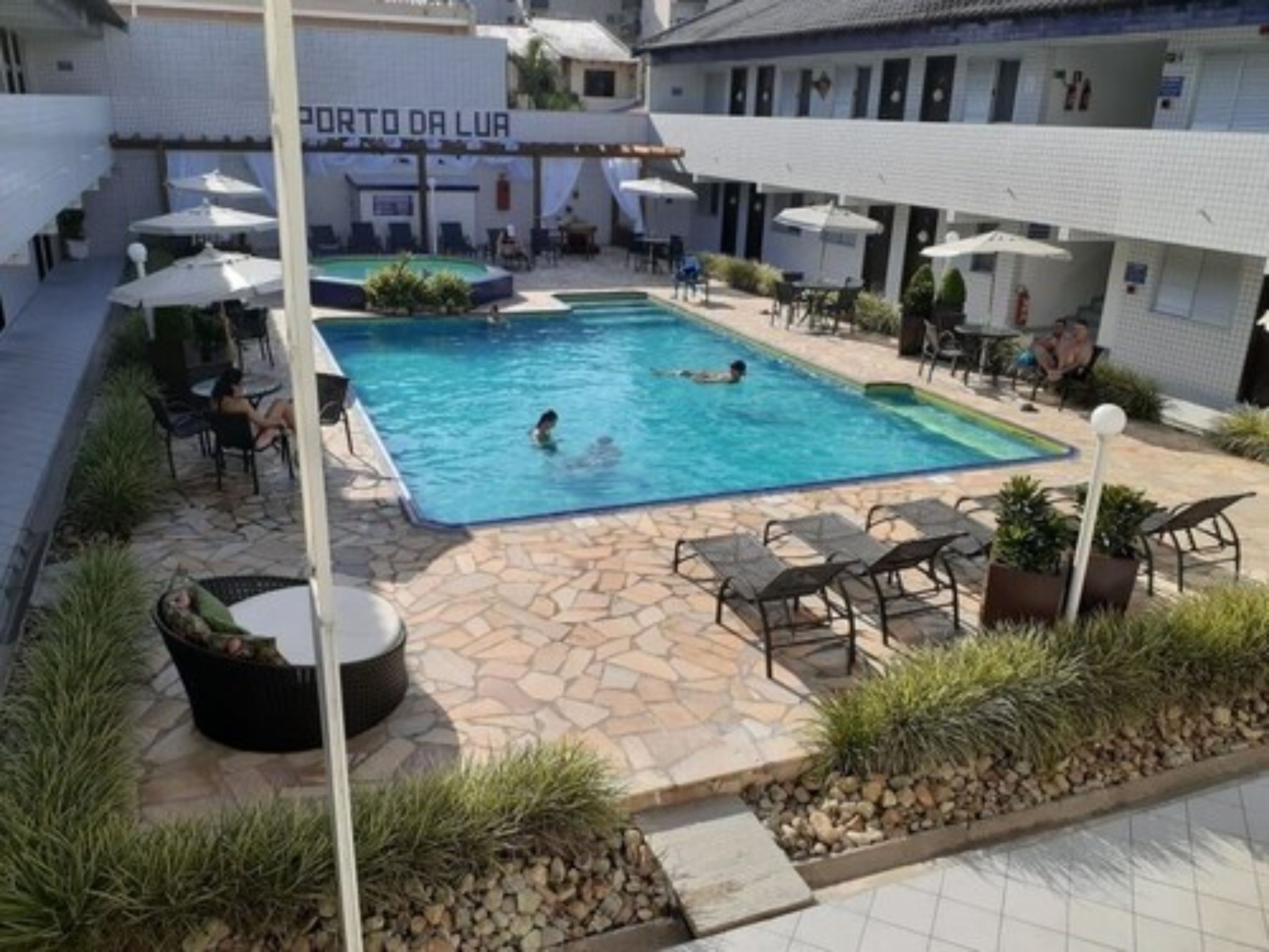 A swimming pool area with lounge chairs and umbrellas, surrounded by a stone patio and a building labeled "PORTO DA LURA".