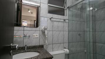 A bathroom with a granite countertop sink, a mirror, a towel rack, a glass shower enclosure, and a toilet.