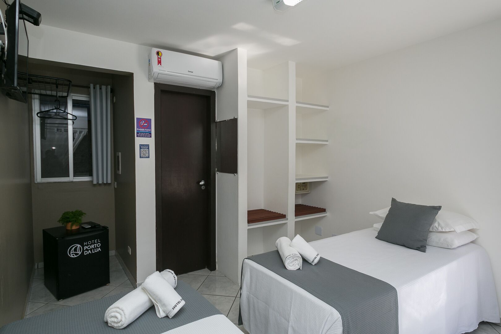 Een hotelkamer met een bed, een bureau met een computer, een televisie, een kledingkast en een kleine plant.