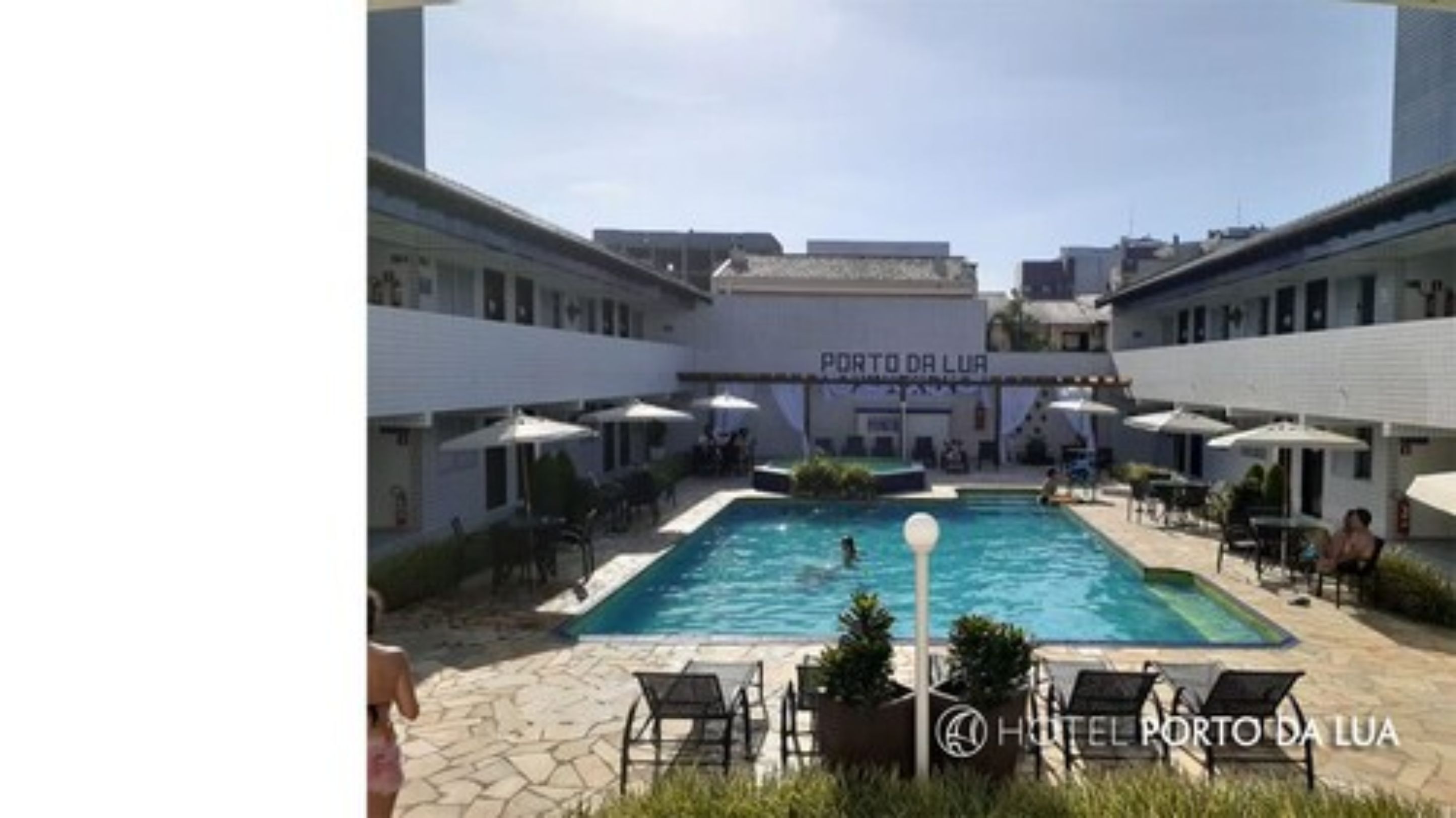 A hotel courtyard with a swimming pool, outdoor seating, and a sign reading "Porto da Lua."