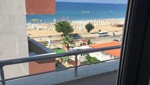 A balcony with a view of a beach, a parked van, and a row of beach umbrellas.