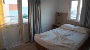 A hotel room with a bed, a nightstand, a lamp, and a view of the sea through the window.