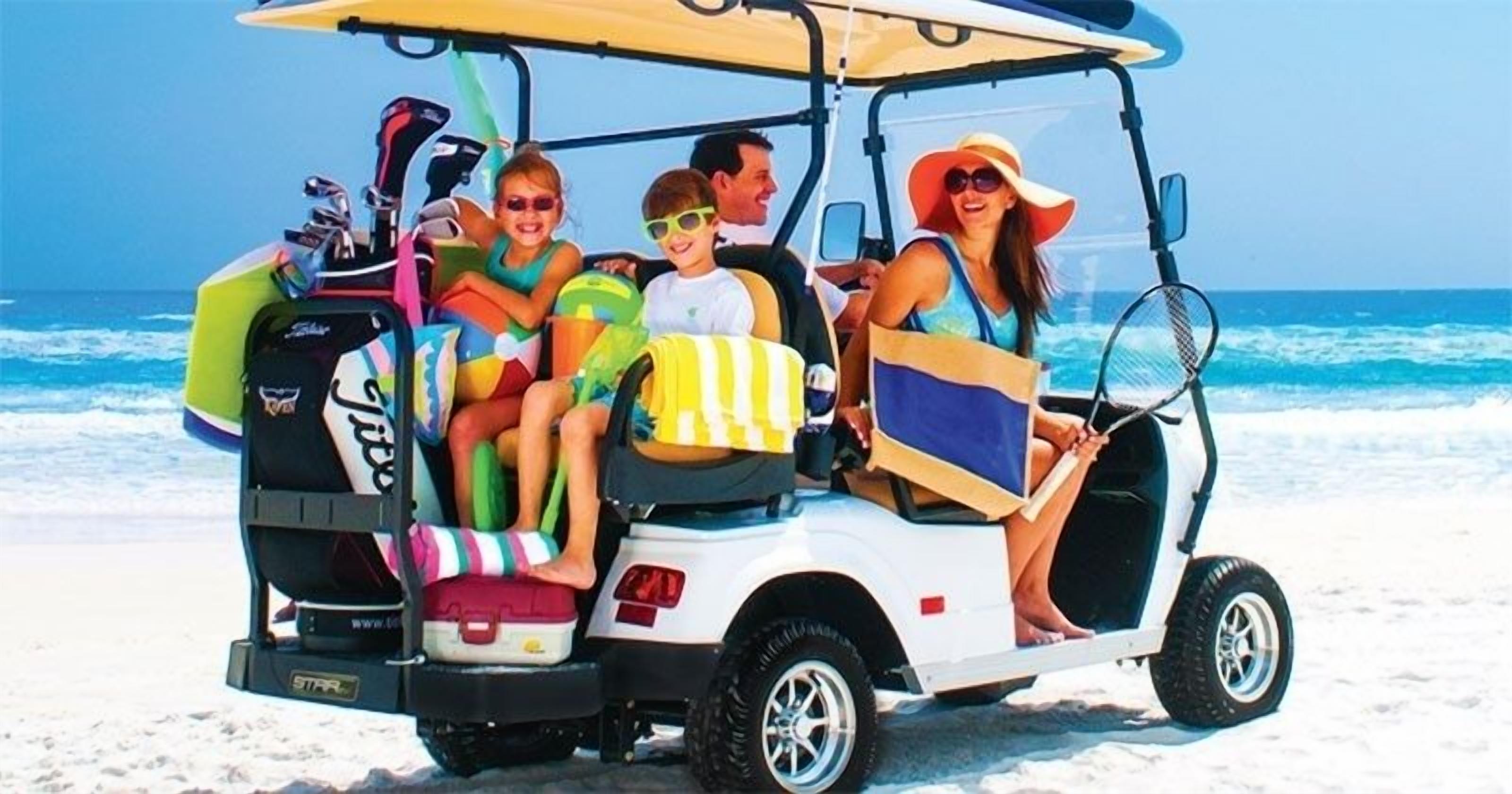 A golf cart on a beach with passengers and luggage.
