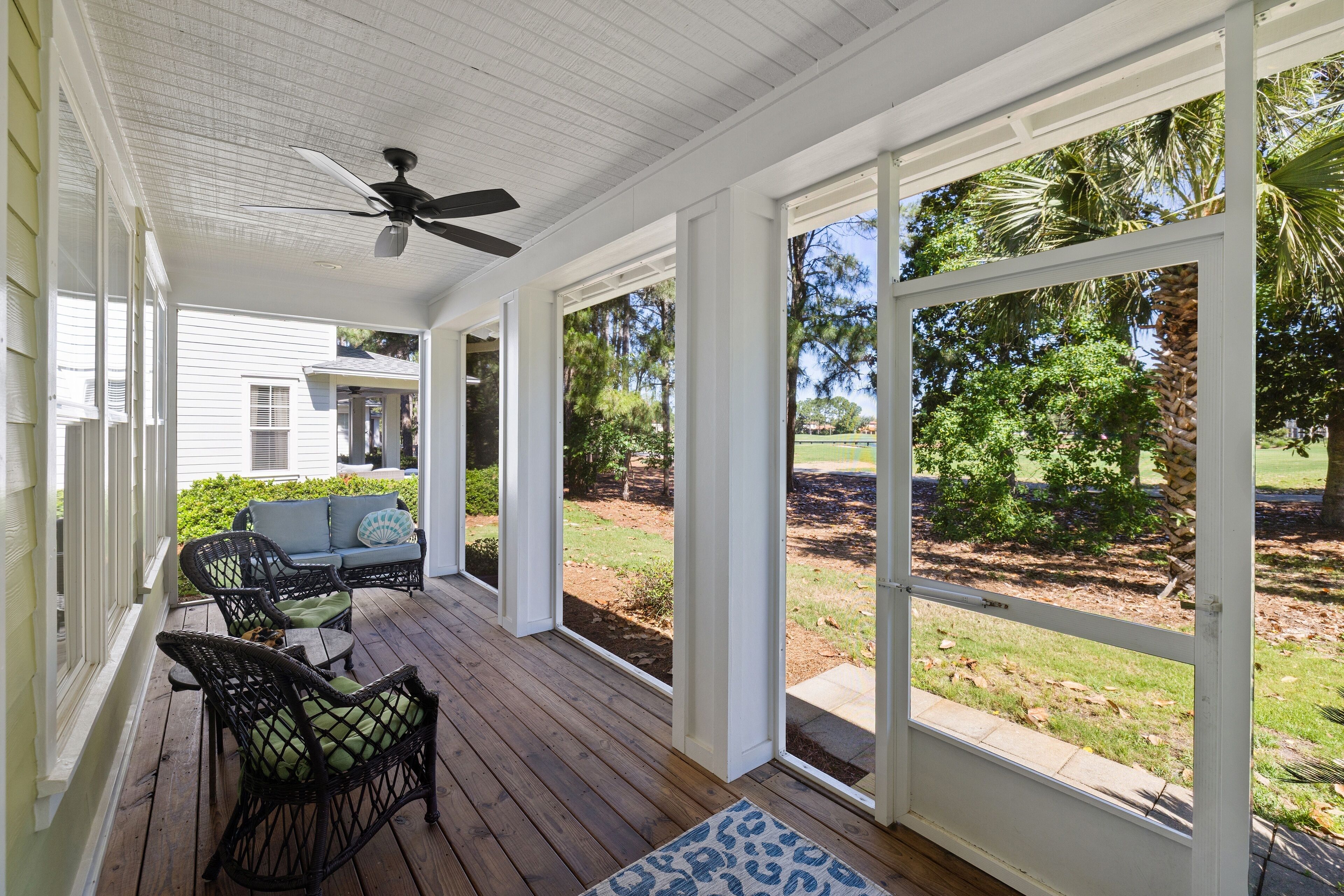 A covered porch with wicker furniture, a ceiling fan, and large windows offering a view of the yard.
