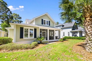 A two-story house with a covered porch, a front yard with a palm tree, and a neighboring house.