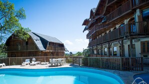 Zona de piscina con edificios de madera, mobiliario exterior y cielo despejado.