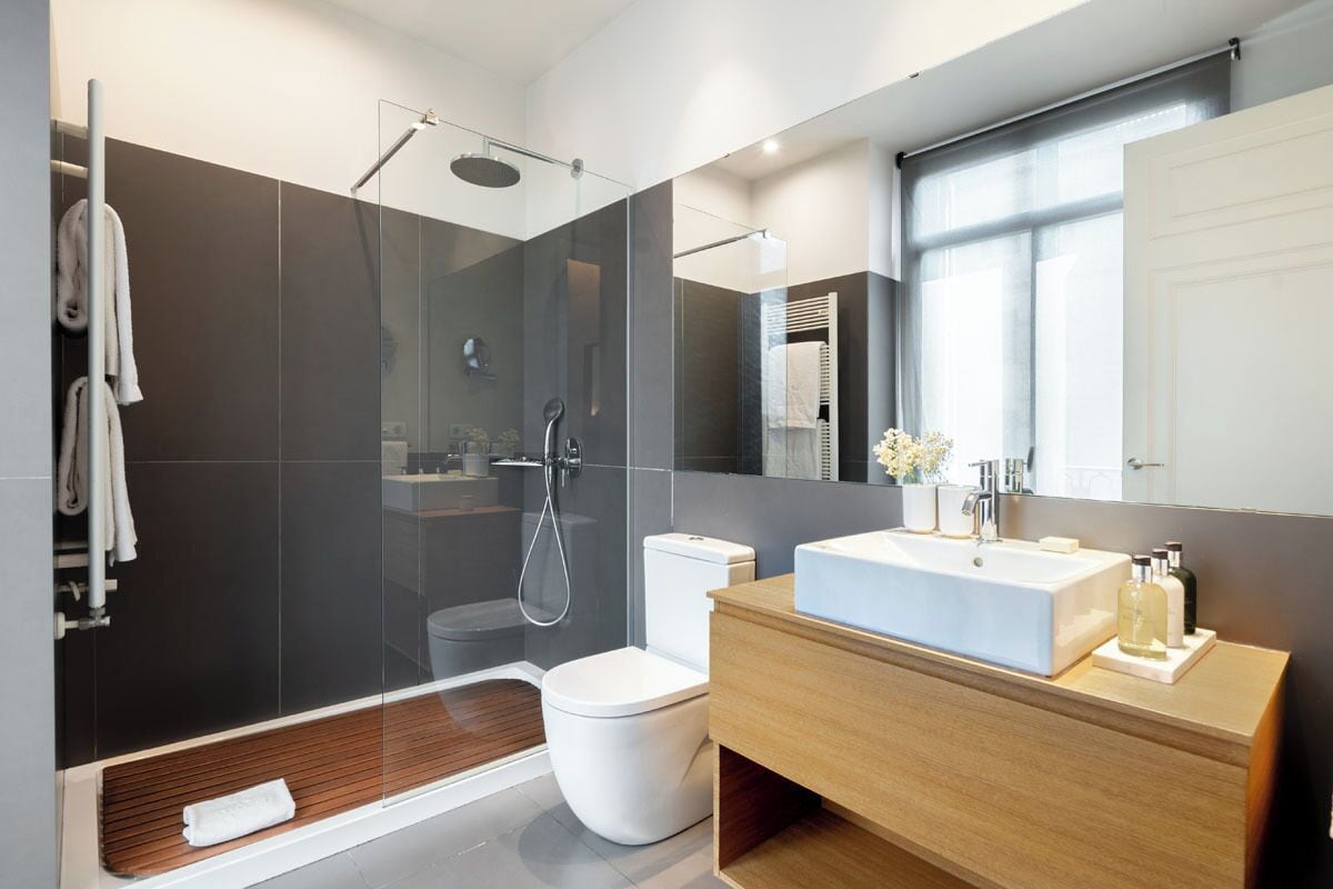 Ein modernes Badezimmer mit einer Duschkabine, einer weißen Toilette, einem hölzernen Waschtisch und einem großen Spiegel.