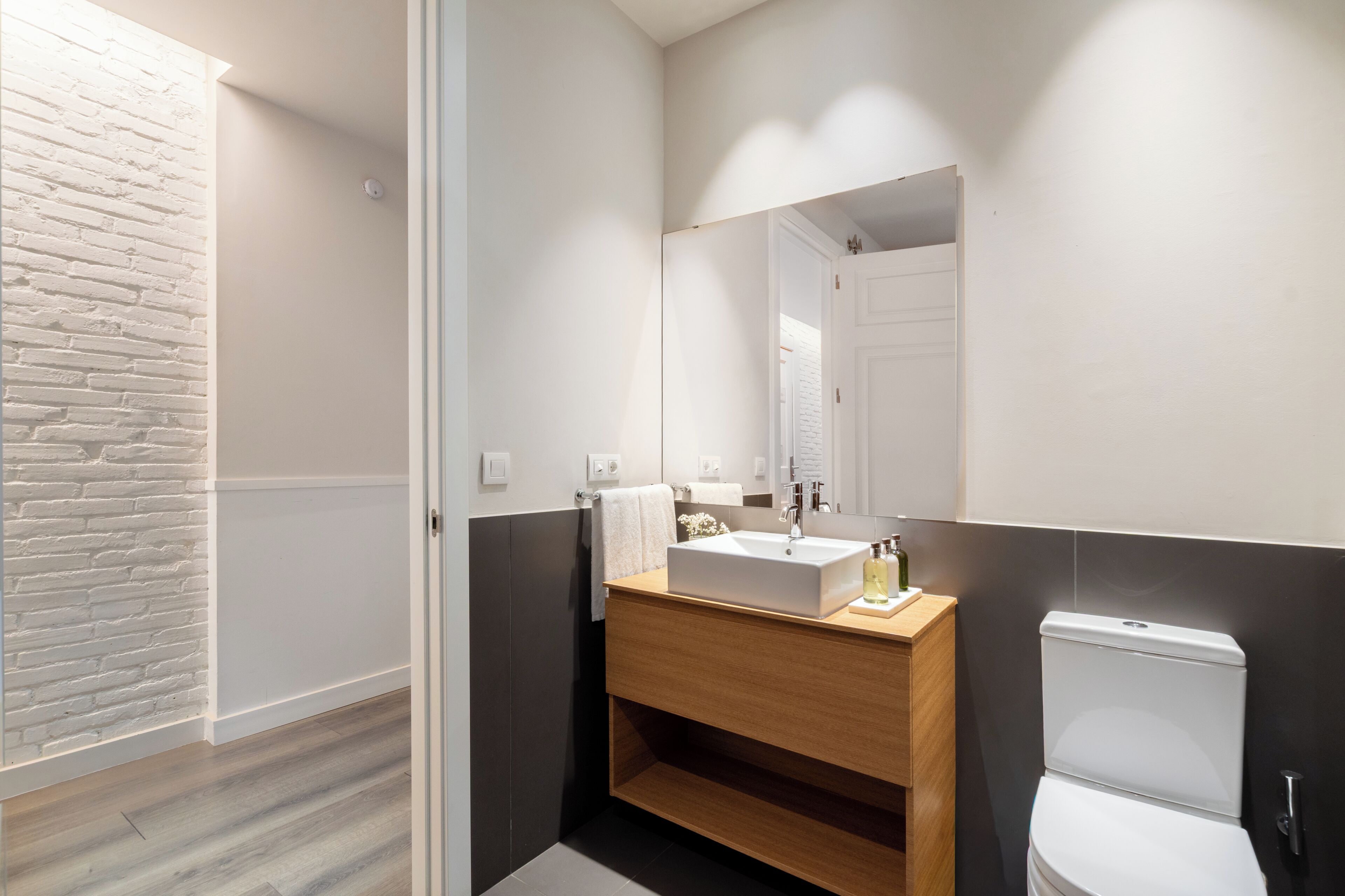 Un baño moderno con lavamanos blanco, tocador de madera y un espejo grande.