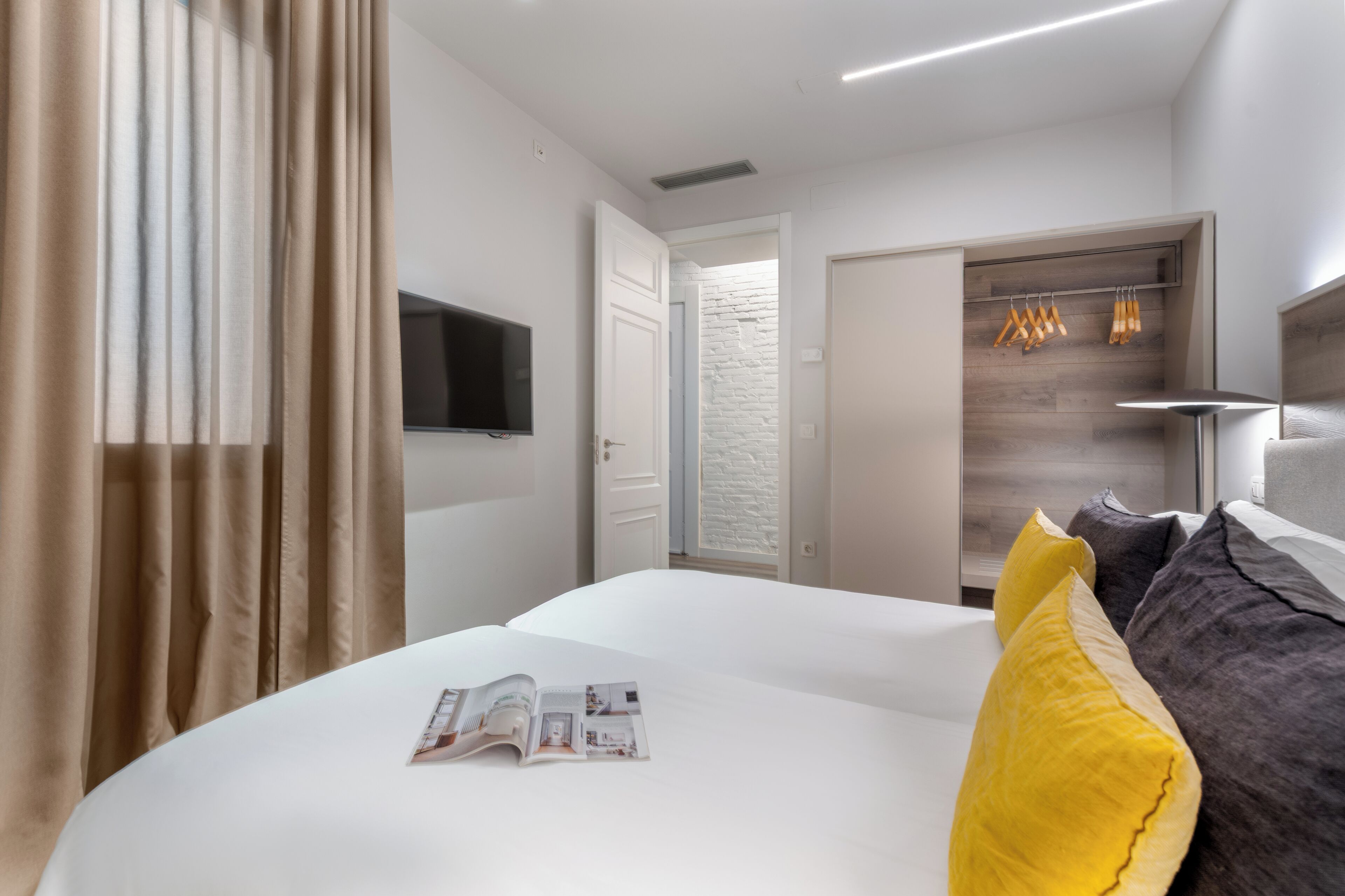 Camera d'albergo con un letto, una TV a schermo piatto, una testiera in legno e una porta che dà su un corridoio.