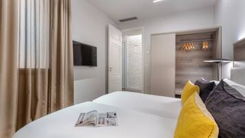 Camera d'albergo con un letto, una TV a schermo piatto, una testiera in legno e una porta che dà su un corridoio.